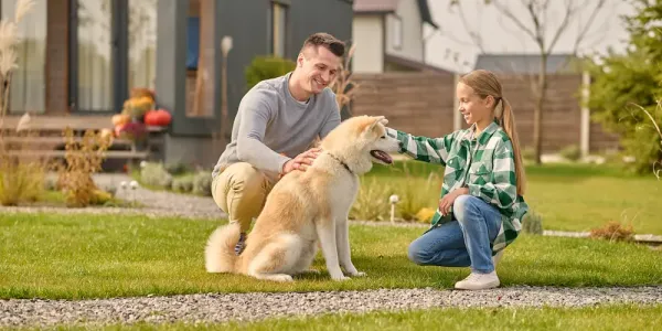 father and daughter petting dog on healthy green lawn